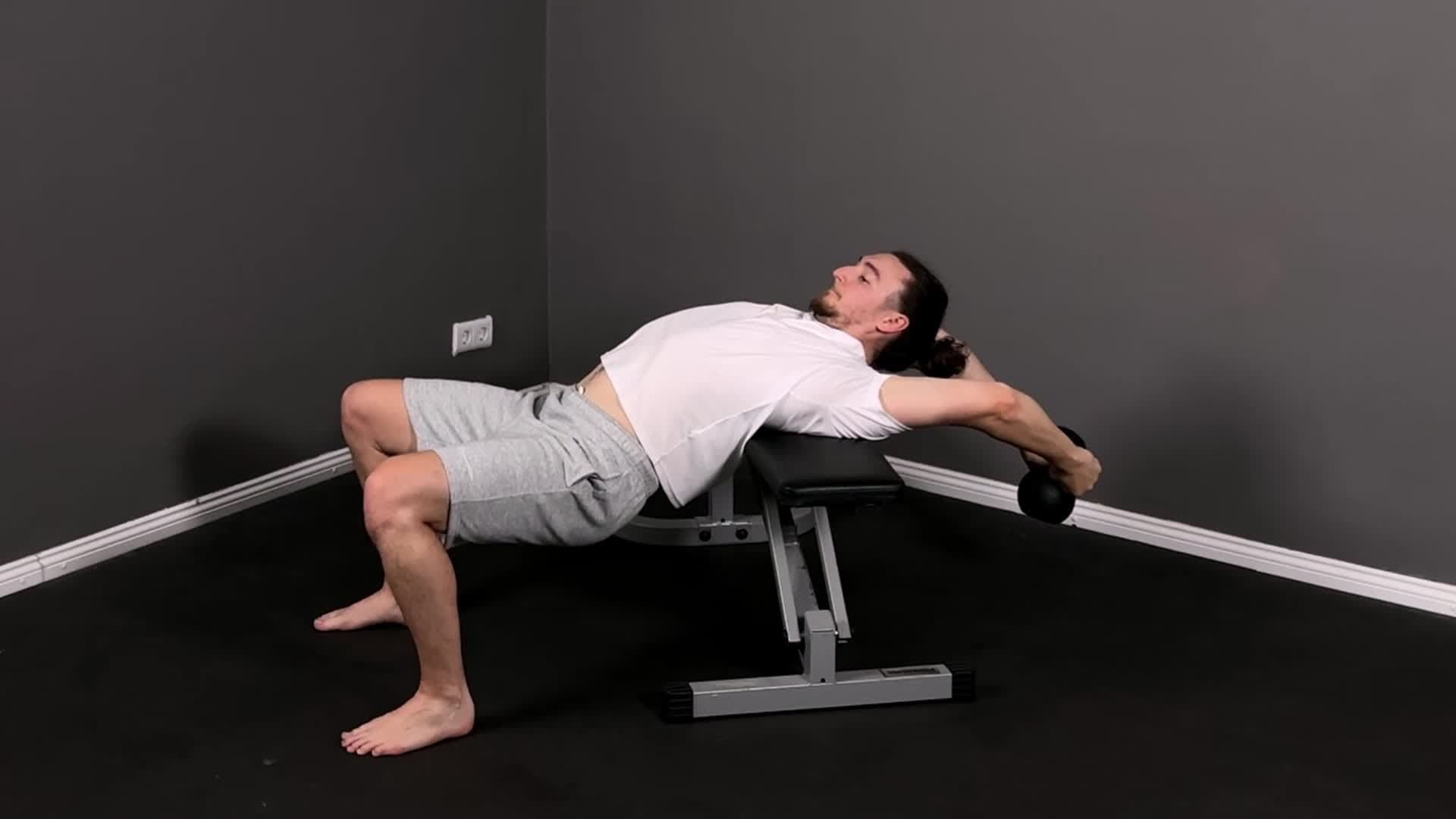 Male athlete performing a deep overhead shoulder mobility drill with arms fully extended, showing controlled shoulder flexibility in a minimalist industrial gym