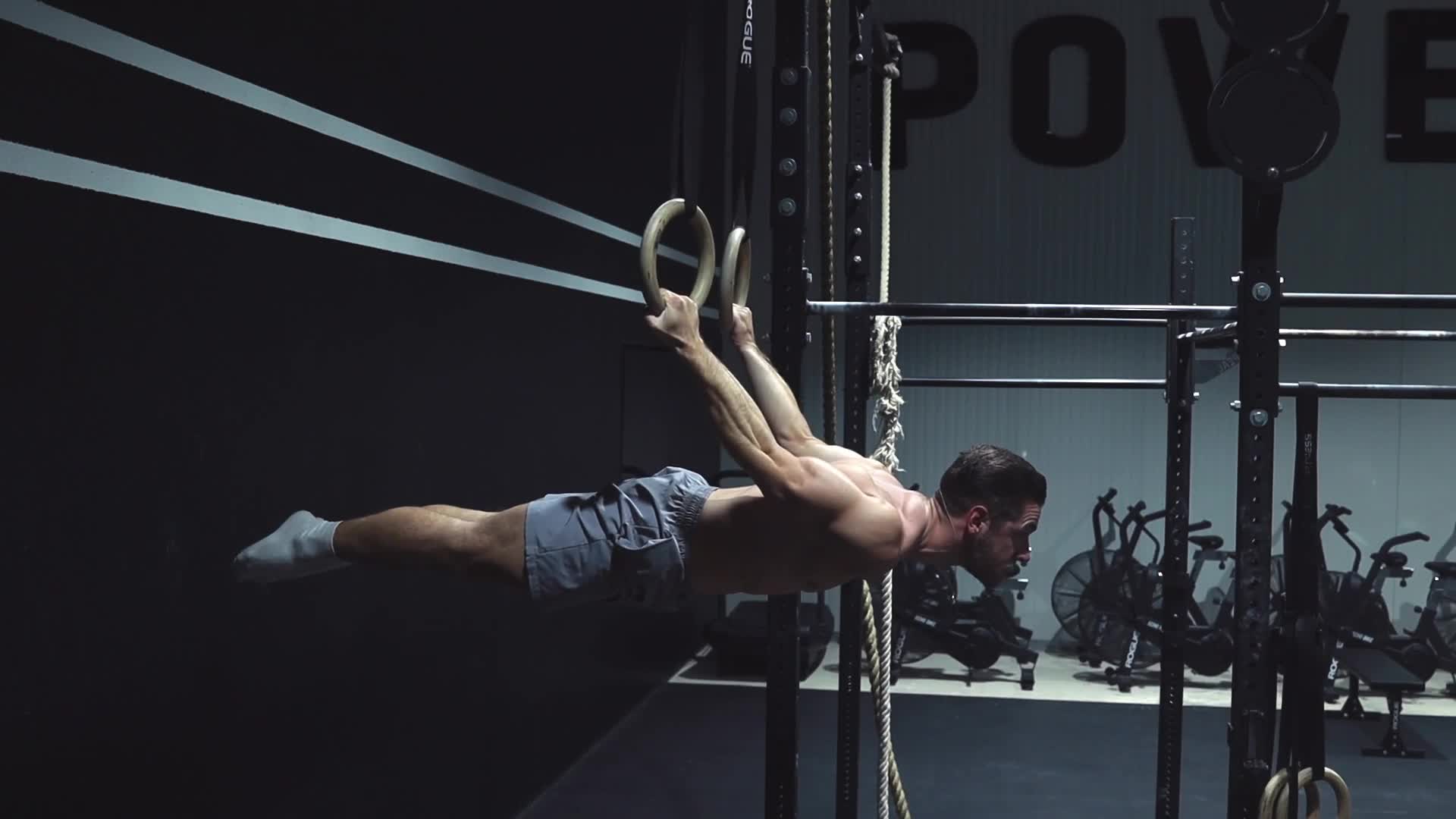 Athlete performing a full back lever on gymnastics rings in a minimalist industrial gym