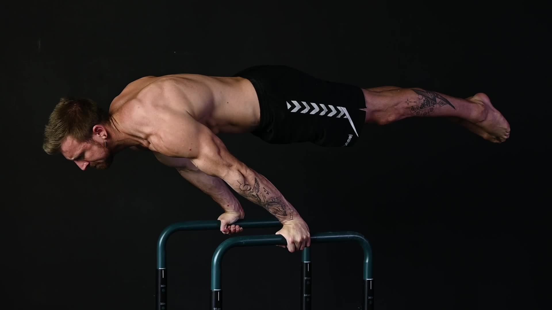 Male athlete performing a strict pull-up in a minimalist gym with concrete walls and black rubber floor mats